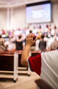 A person raises their hand during a church worship service, symbolizing faith and community.