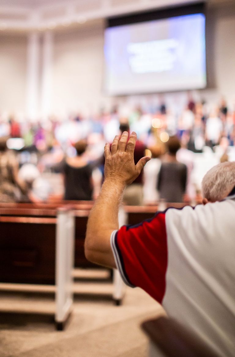 A person raises their hand during a church worship service, symbolizing faith and community.